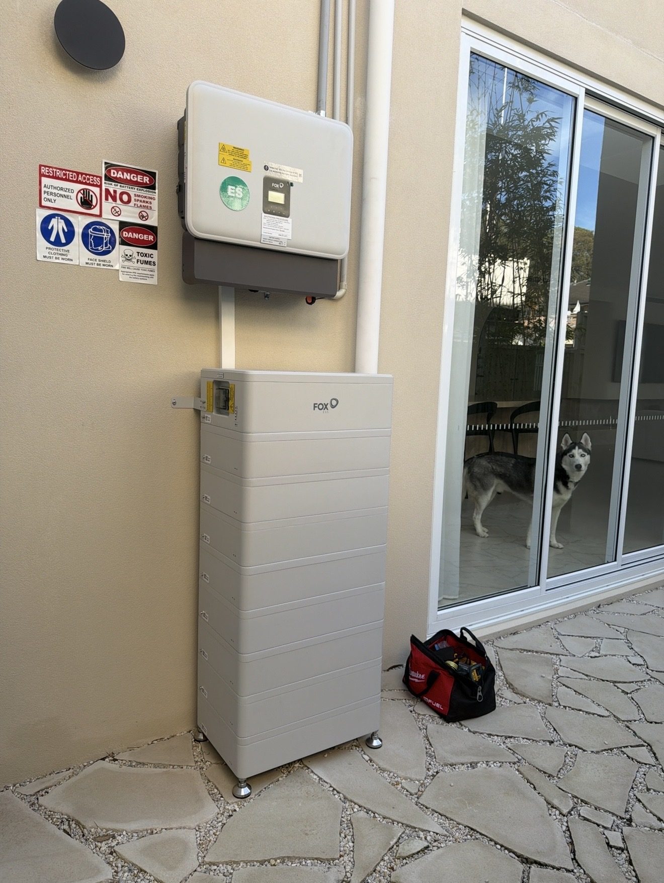 A Fox ESS battery unit installed on an exterior wall with warning signage displayed beside it