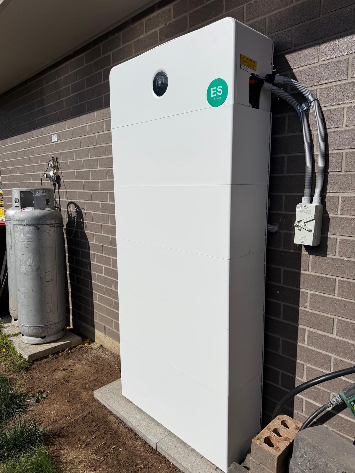 A white battery storage unit installed outside against a brick wall