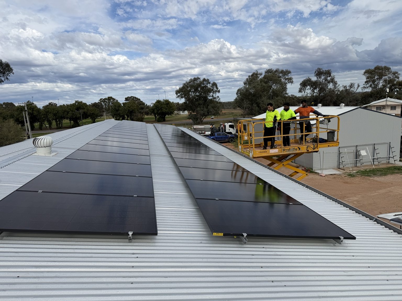 Installers on an elevated work platform beside a completed commercial rooftop solar array