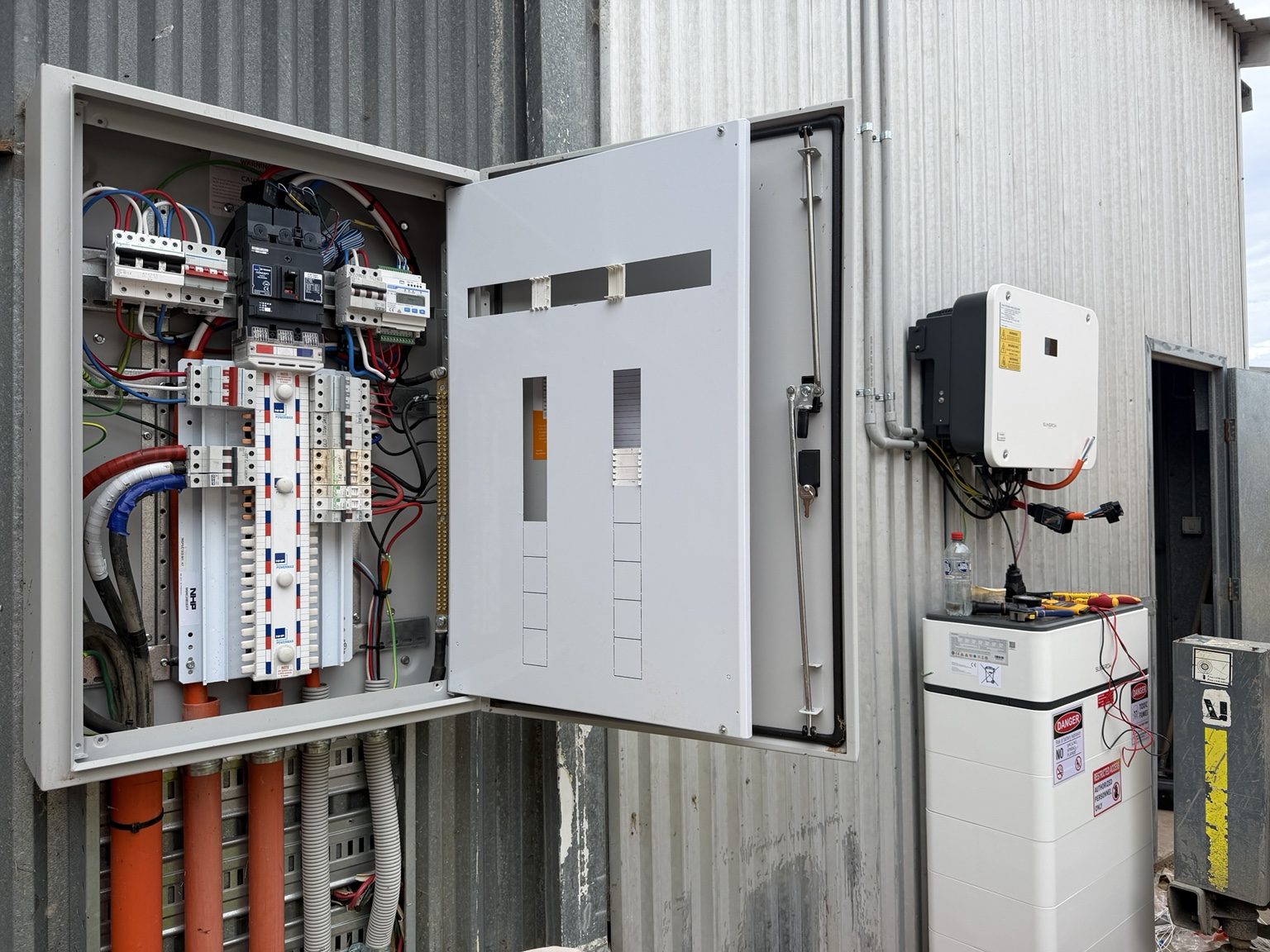 An open commercial switchboard beside a newly installed battery unit during commissioning