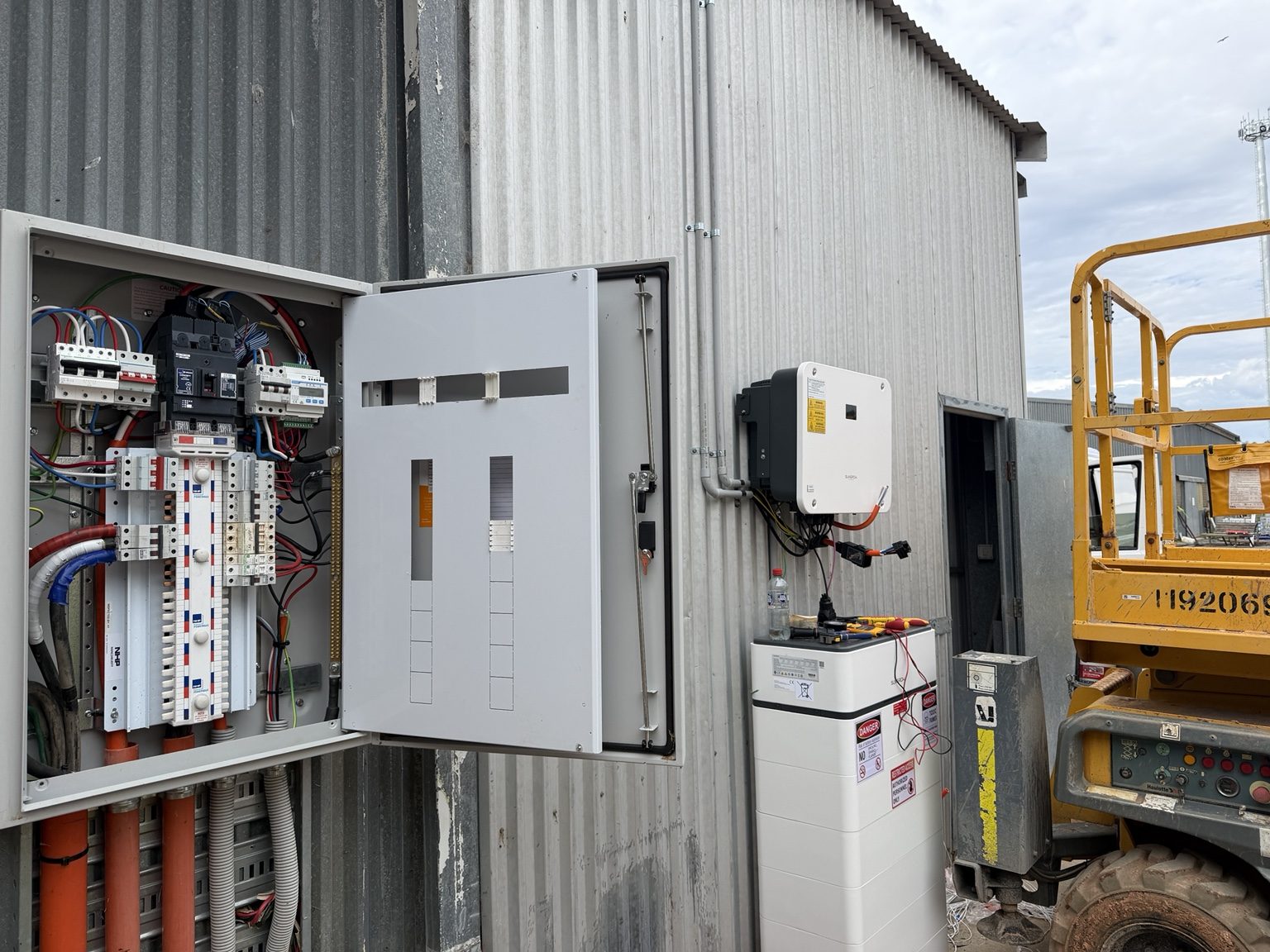 An open commercial switchboard cabinet with wiring visible during installation, beside a solar inverter