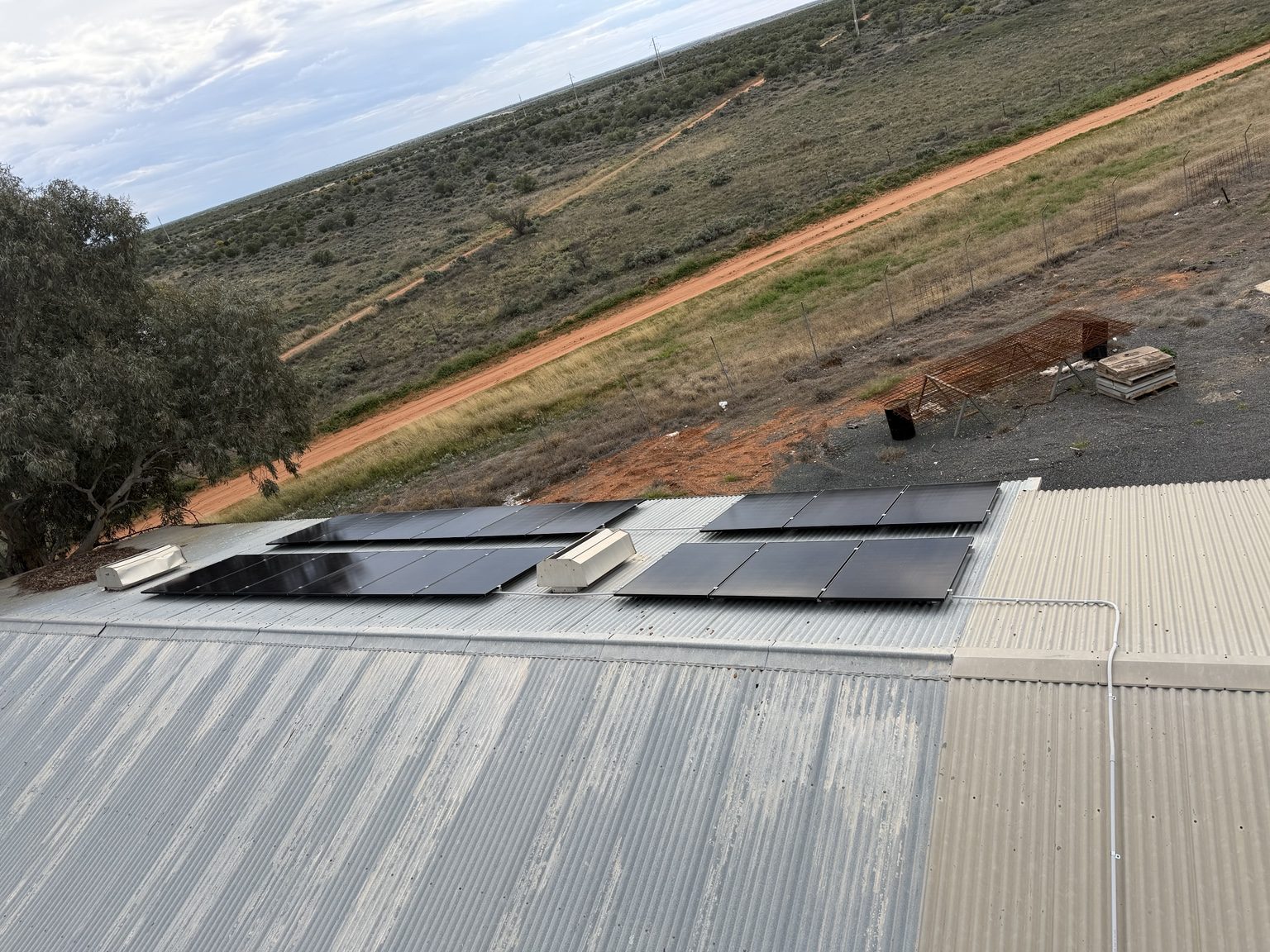 Solar panels installed on a corrugated metal roof beside a red dirt access track